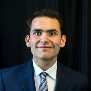A man wearing a business suit poses for a portrait in front of a dark background.